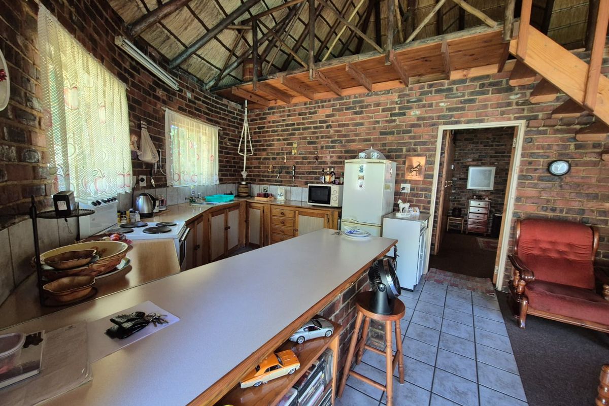 Rustic kitchen featuring exposed brick walls, a high thatched ceiling, wooden staircase, and functional cabinetry with laminate countertops.
