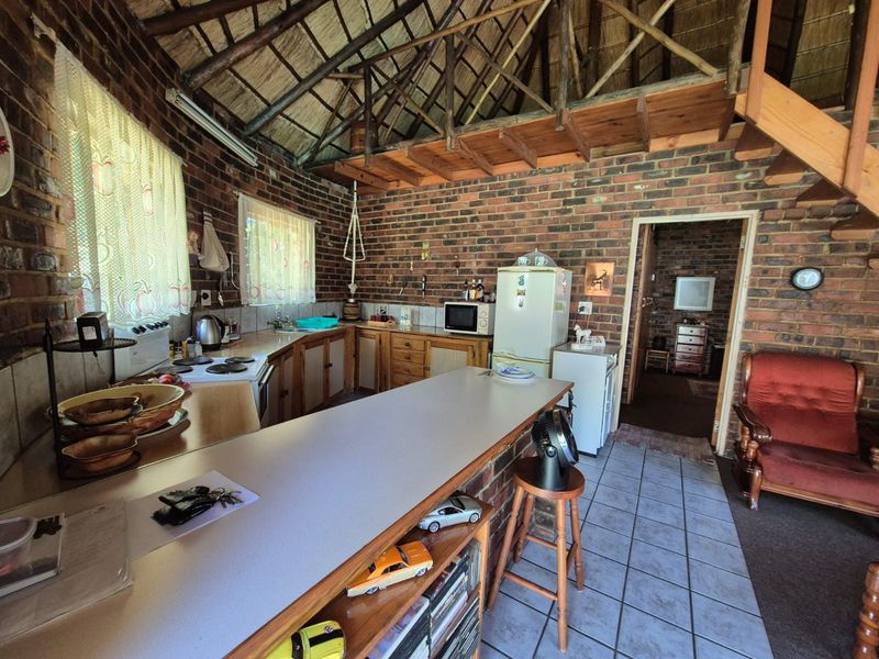Rustic kitchen featuring exposed brick walls, a high thatched ceiling, wooden staircase, and functional cabinetry with laminate countertops.
