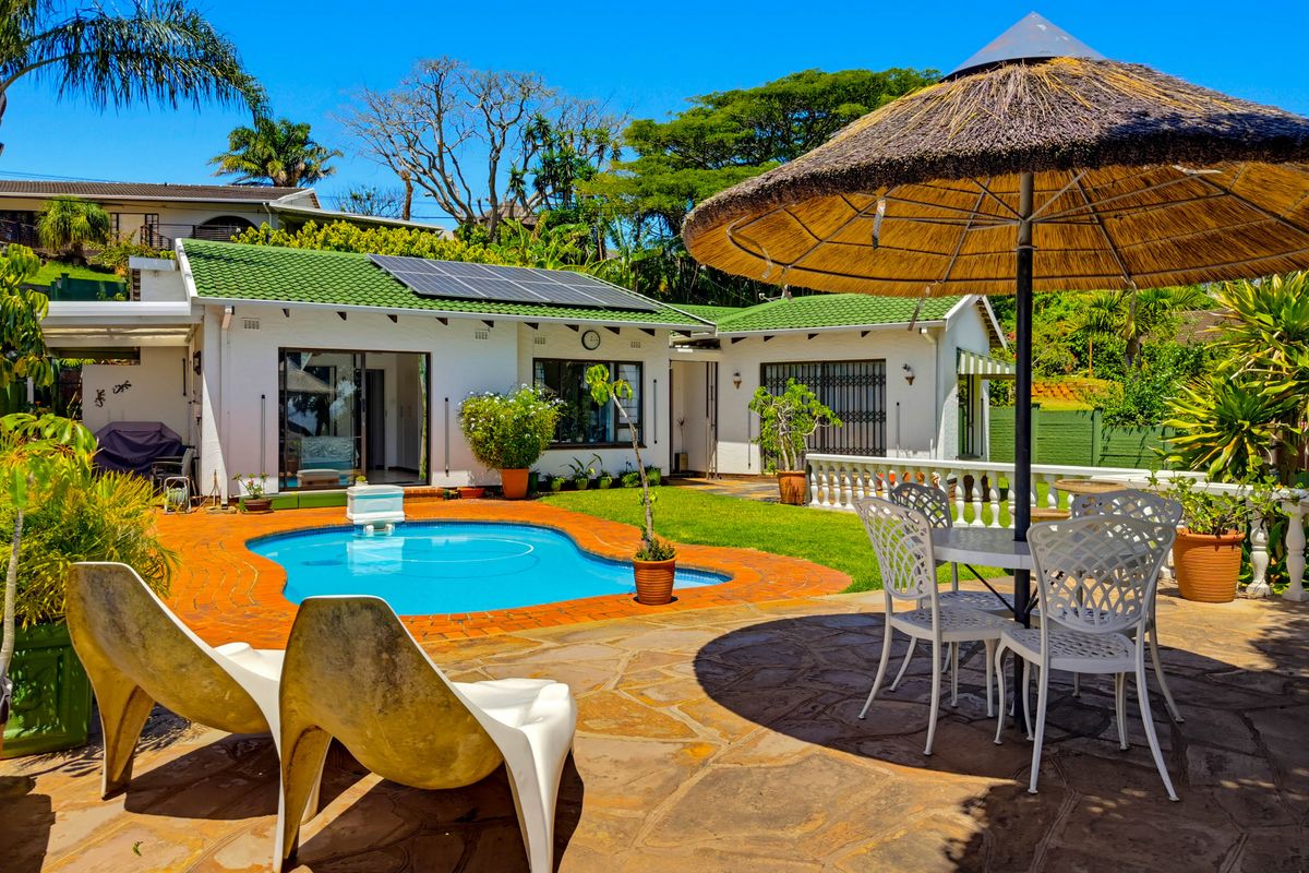 A well-maintained rear garden featuring a swimming pool, paved patio area, and a house with solar panels and a green tiled roof.
