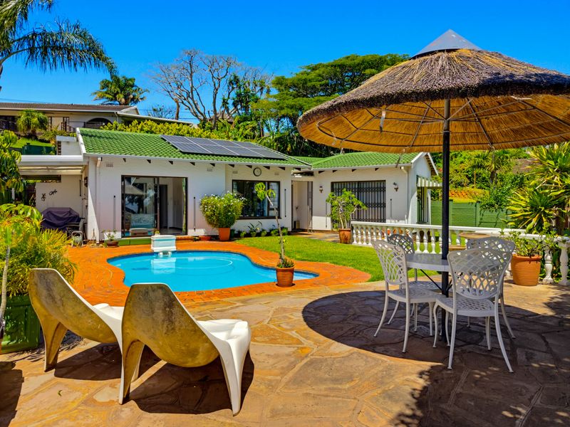 A well-maintained rear garden featuring a swimming pool, paved patio area, and a house with solar panels and a green tiled roof.