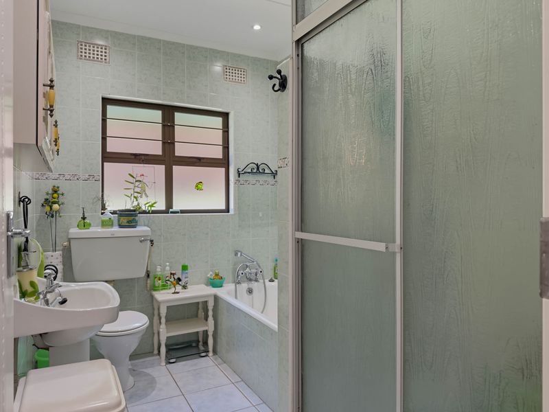 A functional bathroom featuring a pedestal basin, toilet, and a combined bathtub and shower area with light green wall tiling.