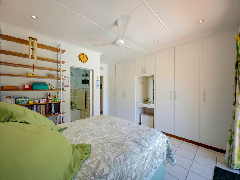 A well-maintained bedroom featuring extensive built-in cabinetry, a dedicated vanity area, tiled flooring, and a ceiling fan with recessed lighting.