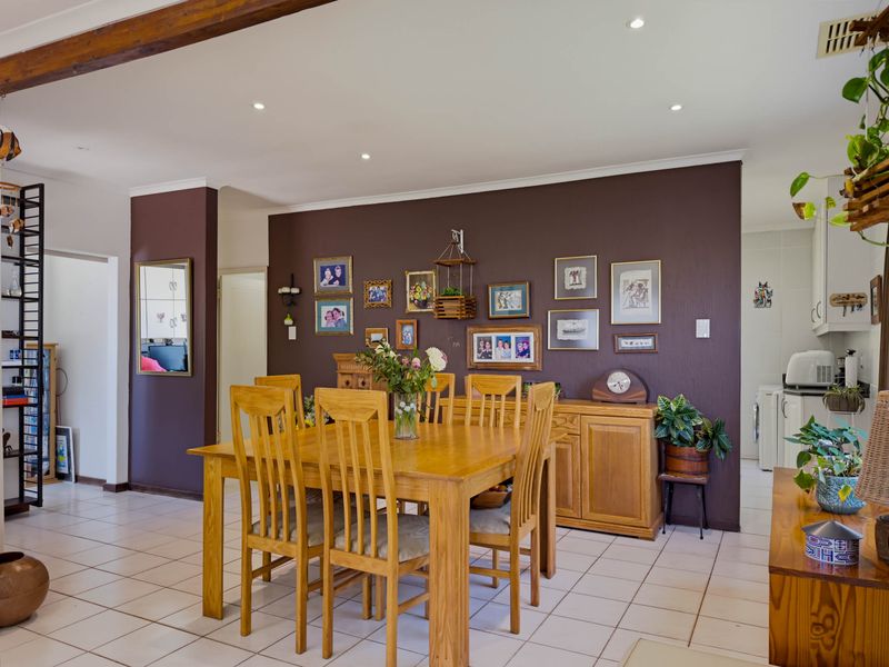 Spacious open-plan dining area featuring tiled flooring, recessed downlighting, and an exposed timber ceiling beam, seamlessly connecting to the adjacent kitchen space.