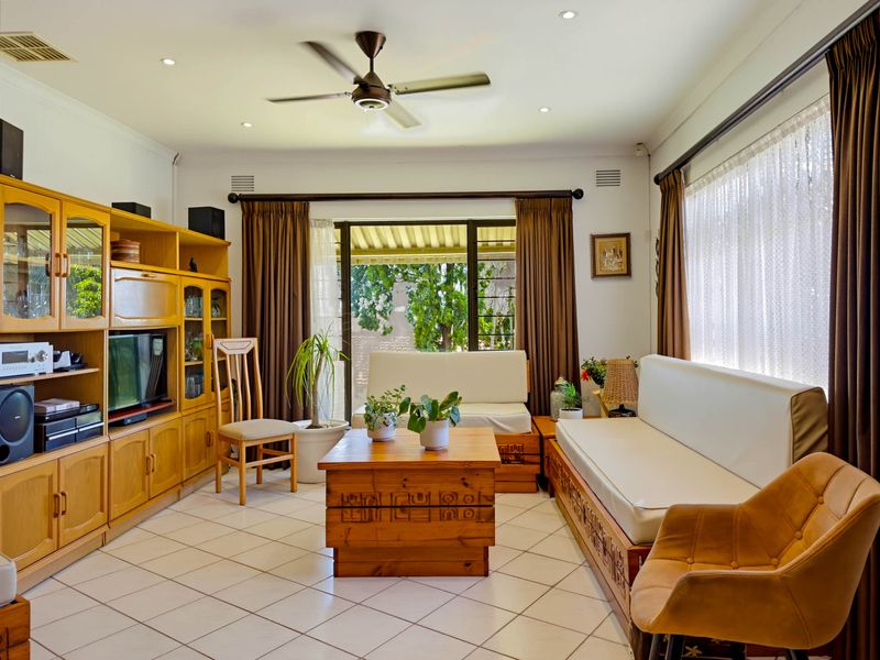 A well-lit living room featuring tiled flooring, a ceiling fan, and large sliding glass doors that provide access to the outdoor area.