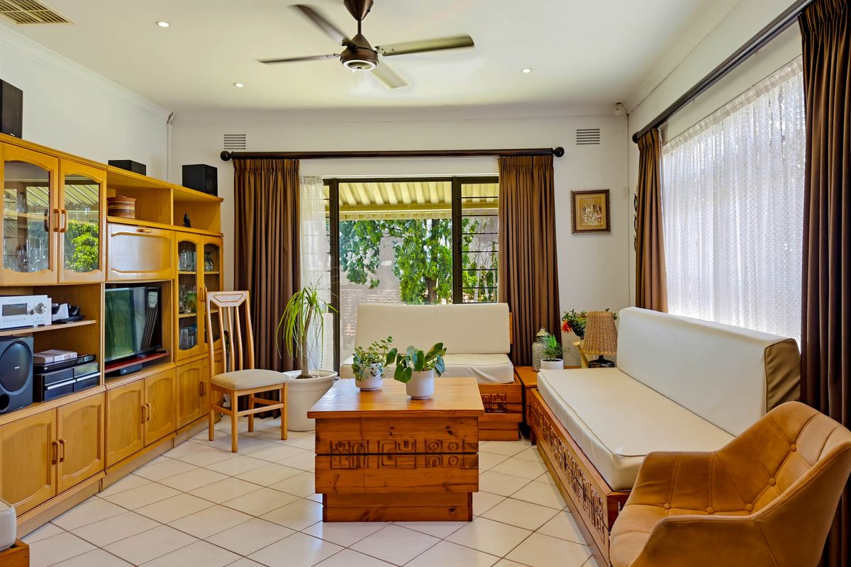 A well-lit living room featuring tiled flooring, a ceiling fan, and large sliding glass doors that provide access to the outdoor area.