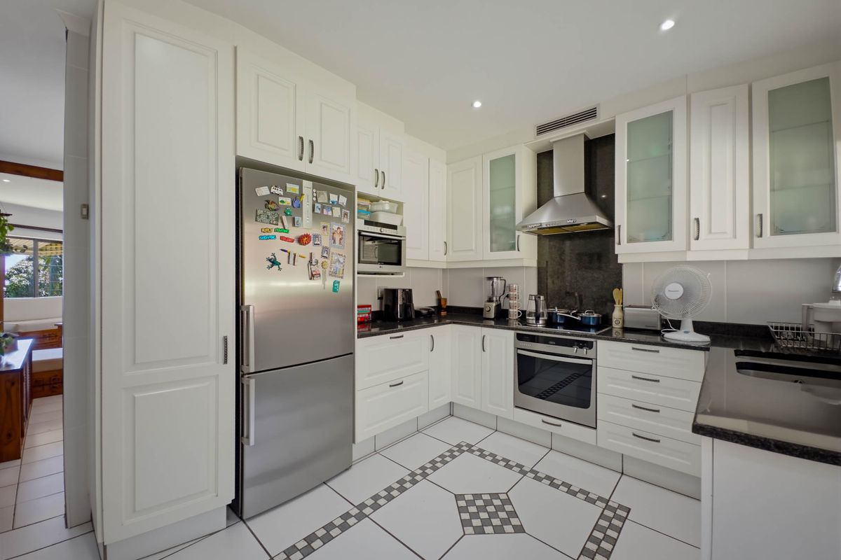 A well-maintained kitchen featuring white cabinetry, granite countertops, stainless steel appliances, and decorative tiled flooring with recessed lighting.