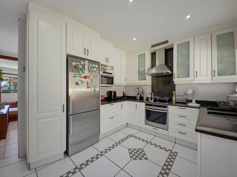 A well-maintained kitchen featuring white cabinetry, granite countertops, stainless steel appliances, and decorative tiled flooring with recessed lighting.