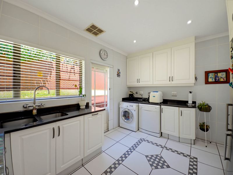 A functional laundry room featuring white cabinetry, dark granite countertops, an undermount sink, and tiled flooring with decorative inlay.