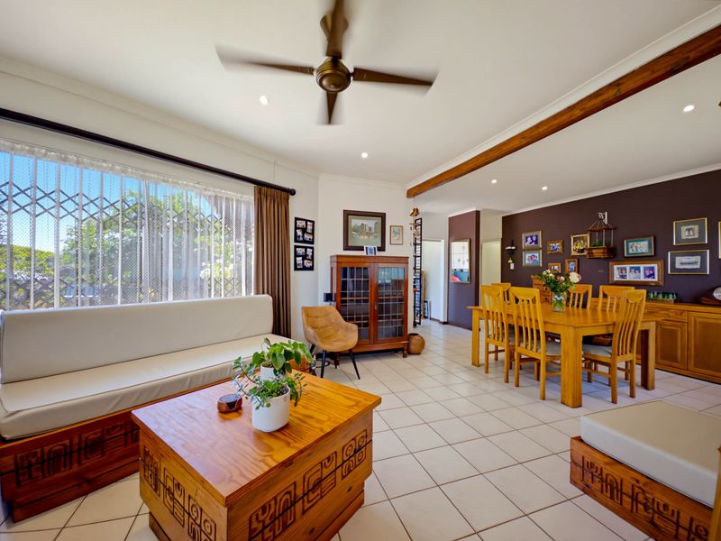Spacious open-plan living and dining area featuring tiled flooring, a ceiling fan, and an exposed timber beam, offering a functional layout for family living.