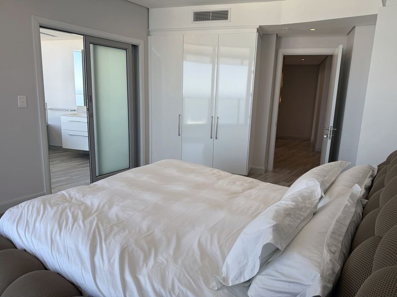 A modern bedroom featuring built-in high-gloss wardrobes, ducted air conditioning, and direct access to an en-suite bathroom through a sliding glass door.
