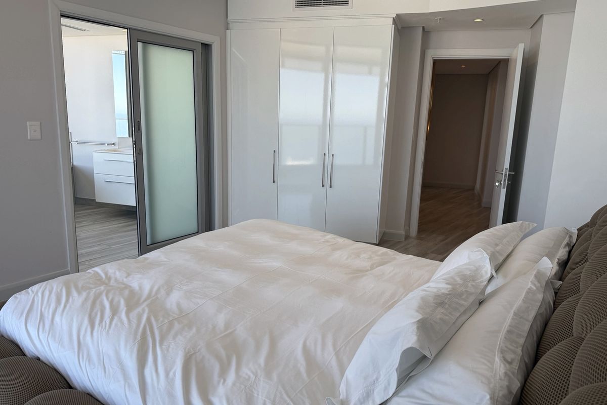 A modern bedroom featuring built-in high-gloss wardrobes, ducted air conditioning, and direct access to an en-suite bathroom through a sliding glass door.