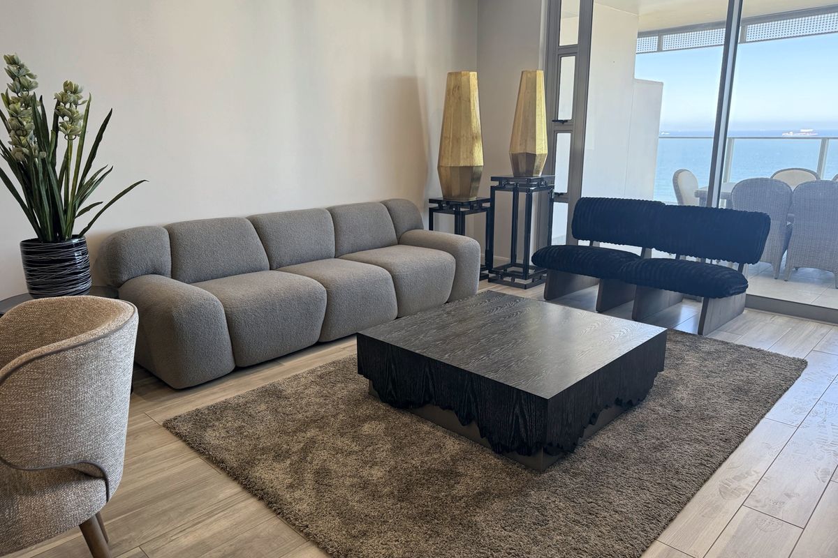 A bright living room featuring modern tiled flooring and large sliding glass doors that provide access to a balcony with ocean views.