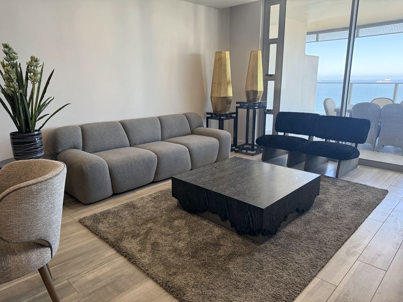 A bright living room featuring modern tiled flooring and large sliding glass doors that provide access to a balcony with ocean views.