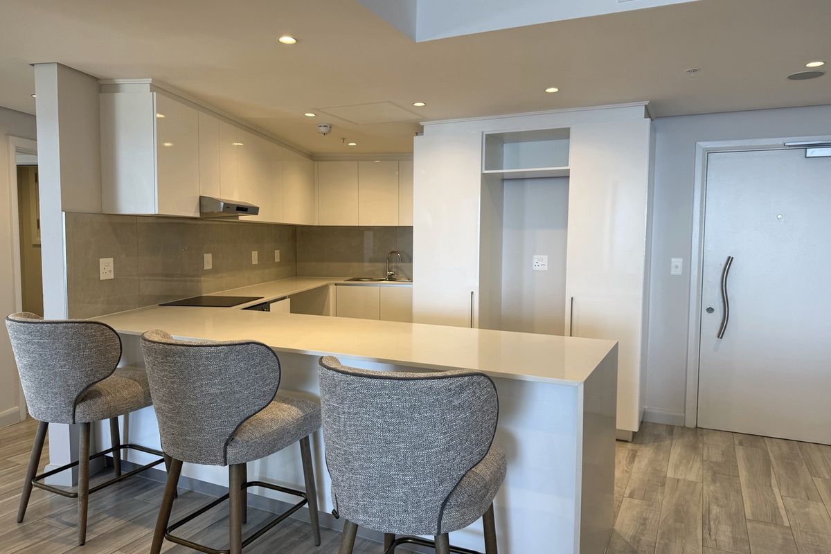Modern kitchen featuring sleek white cabinetry, stone countertops, an integrated breakfast bar, and high-quality built-in appliances in a contemporary open-plan layout.