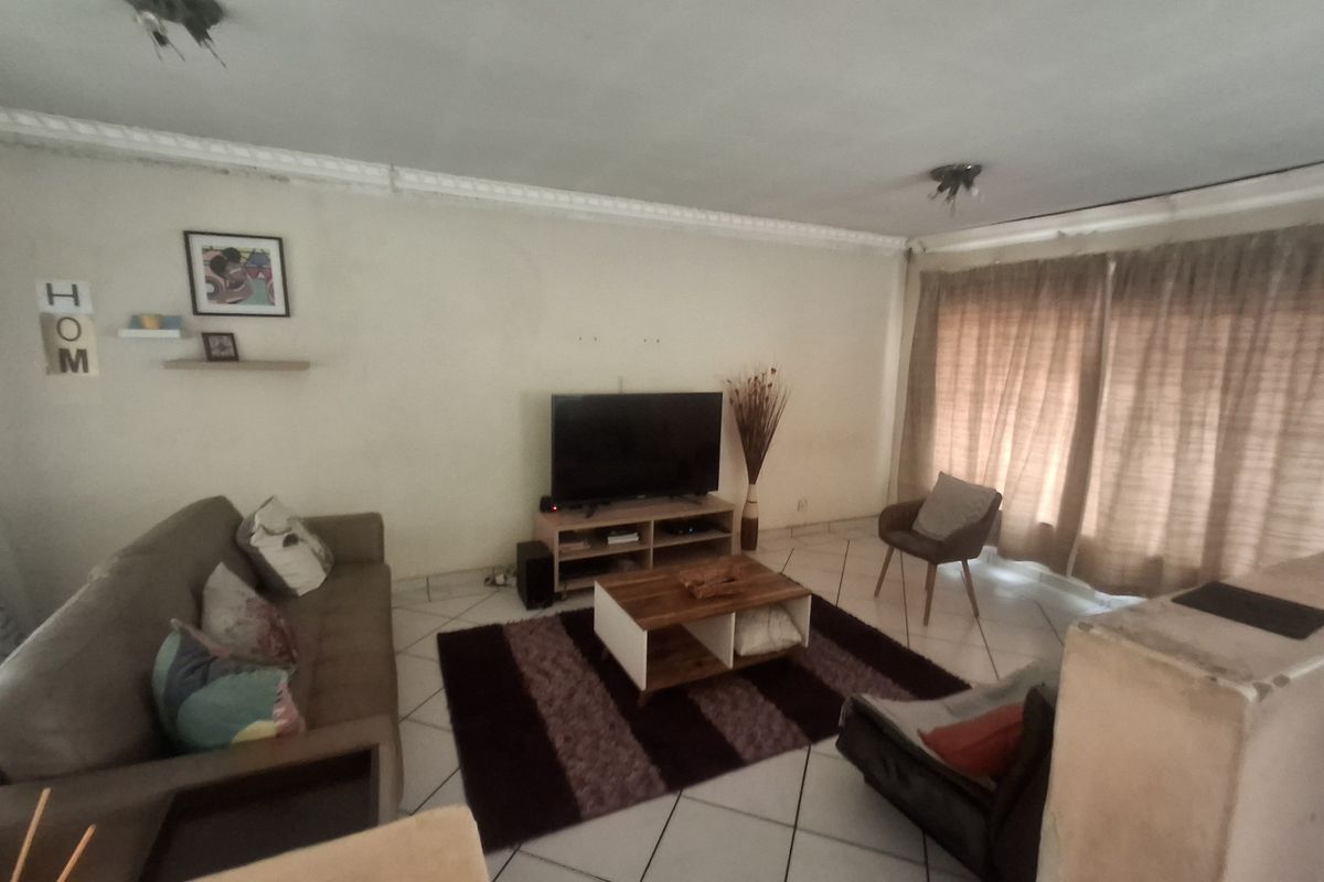 A living room featuring tiled flooring and decorative ceiling cornicing, currently showing signs of wear and requiring cosmetic updates.