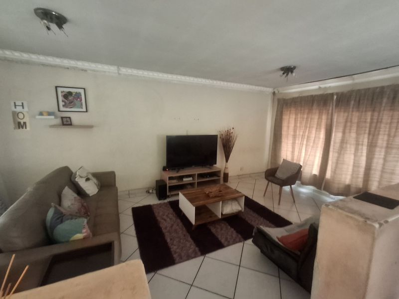 A living room featuring tiled flooring and decorative ceiling cornicing, currently showing signs of wear and requiring cosmetic updates.