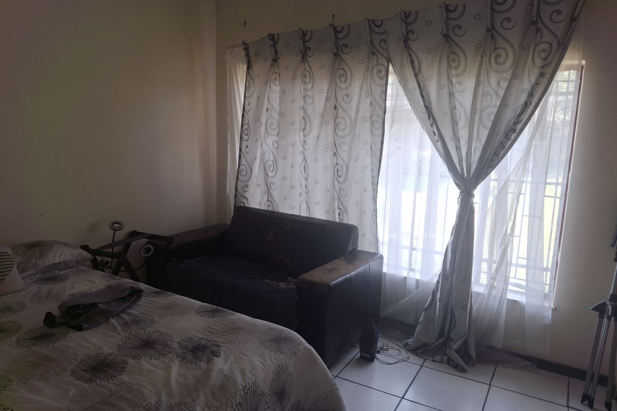 A bedroom featuring tiled flooring and a large window with security bars, providing natural light.