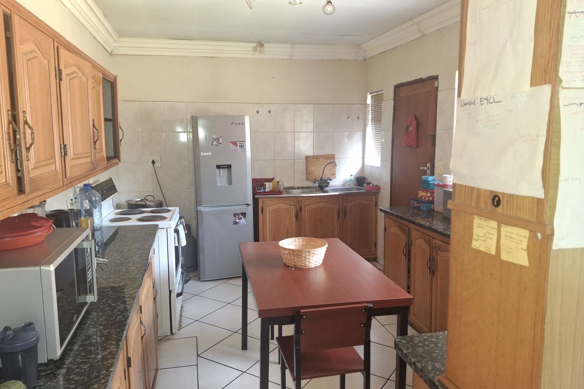 A functional kitchen featuring wooden cabinetry, granite countertops, tiled splashbacks, and tiled flooring, offering a practical layout with potential for modern updates.