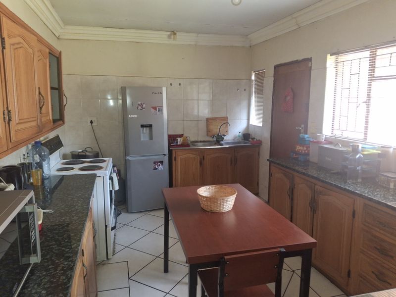A functional kitchen featuring wooden cabinetry, granite countertops, tiled flooring, and an electric stove, offering potential for modernization and cosmetic updates.