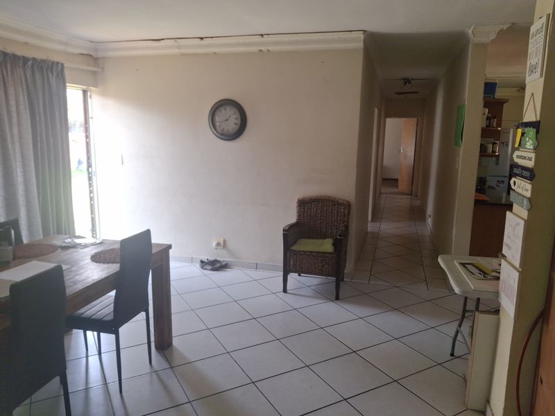 Open plan living area featuring tiled flooring and access to the exterior, showing signs of wear on the walls and ceiling cornicing.