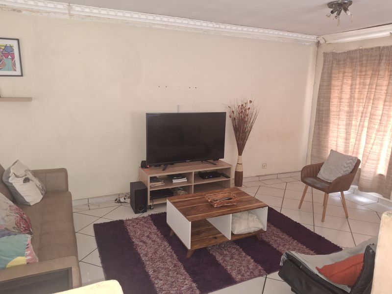 A living room featuring tiled flooring and decorative ceiling cornicing, currently showing signs of wear on the walls and ceiling.