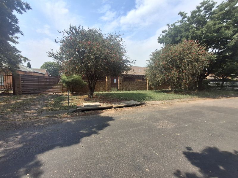 Street view of the property frontage featuring a brick boundary wall, metal gates, and established trees along the verge.