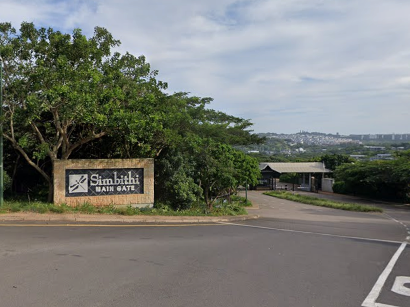 View of the main entrance gate to the Simbithi estate, featuring a stone signage wall and paved access road.