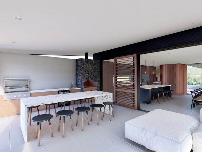 A modern covered patio featuring a built-in braai, stone-clad fireplace, and a marble-topped island, seamlessly connecting to the indoor living area.