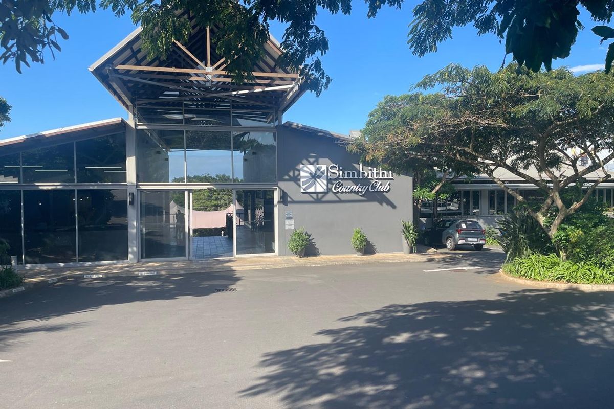Front exterior view of the Simbithi Country Club featuring a modern architectural design with glass facade and timber roof structure.
