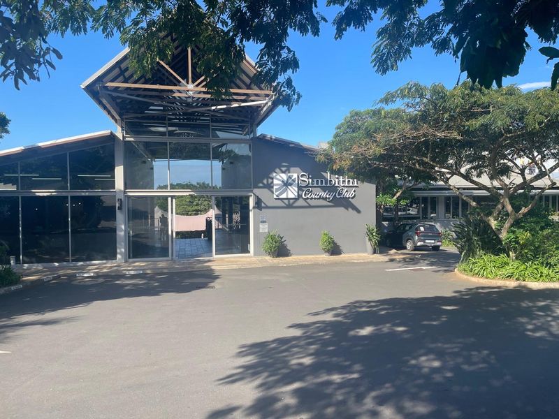 Front exterior view of the Simbithi Country Club featuring a modern architectural design with glass facade and timber roof structure.