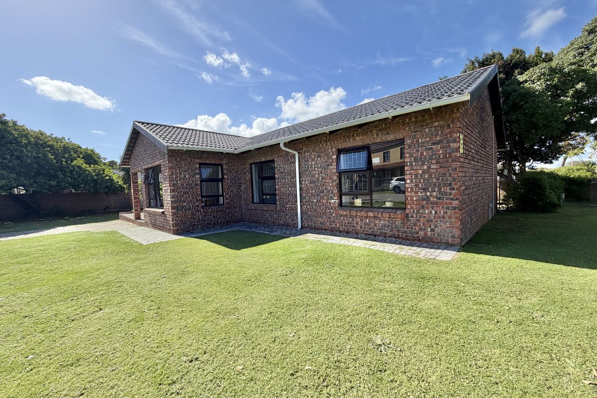 A well-maintained face brick house exterior featuring a tiled roof, aluminium window frames, and a neat surrounding lawn with paved pathways.