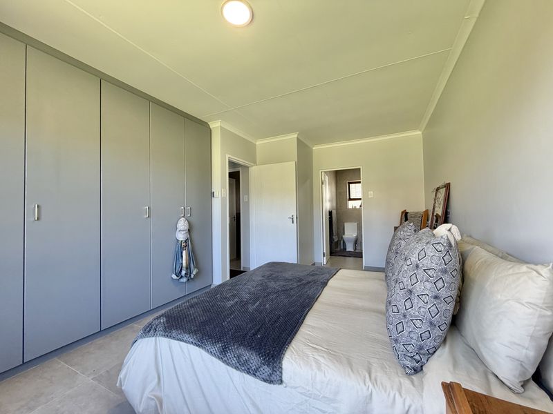 A well-maintained bedroom featuring extensive built-in cupboards, neutral tiled flooring, and direct access to an en-suite bathroom.