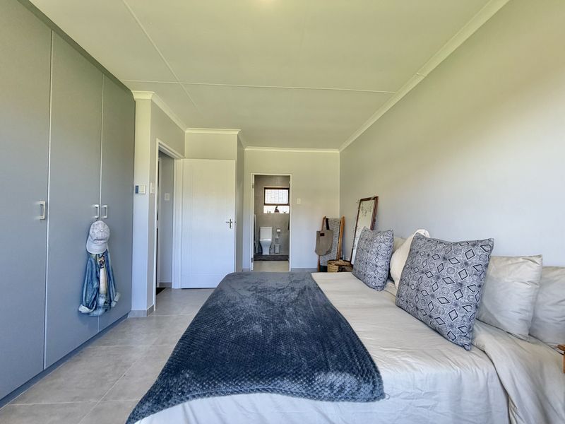 A well-maintained bedroom featuring neutral tiled flooring, ample built-in cupboard space, and direct access to an en-suite bathroom.