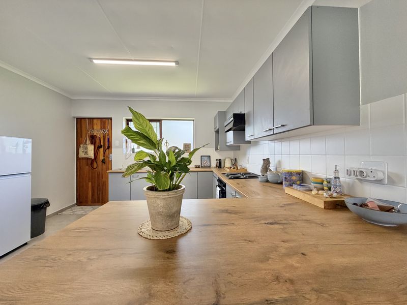 A modern kitchen featuring grey cabinetry, wood-look laminate countertops, a tiled backsplash, and integrated appliances, offering a clean and functional workspace.