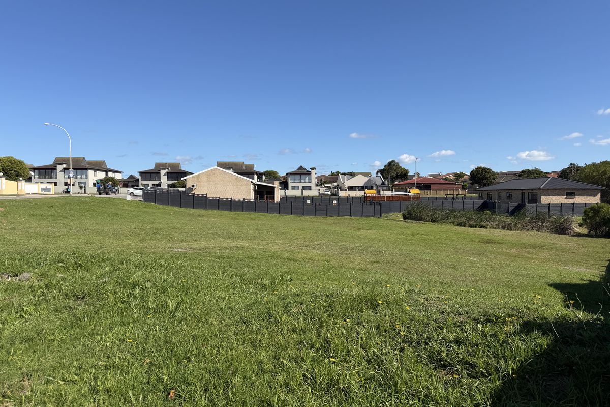 A vacant residential plot featuring a well-maintained grass lawn and perimeter fencing, situated in a developed suburban neighborhood.