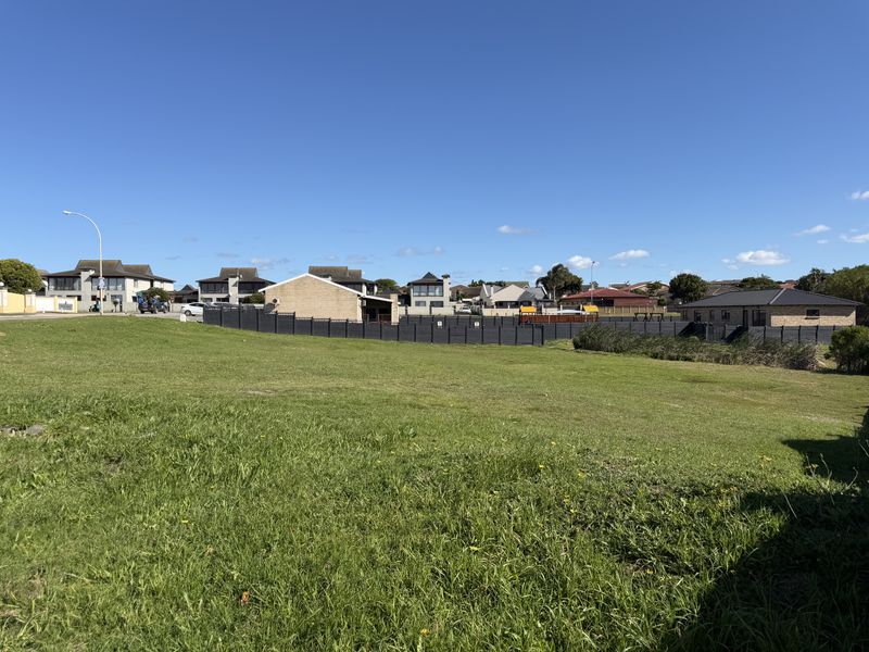 A vacant residential plot featuring a well-maintained grass lawn and perimeter fencing, situated in a developed suburban neighborhood.