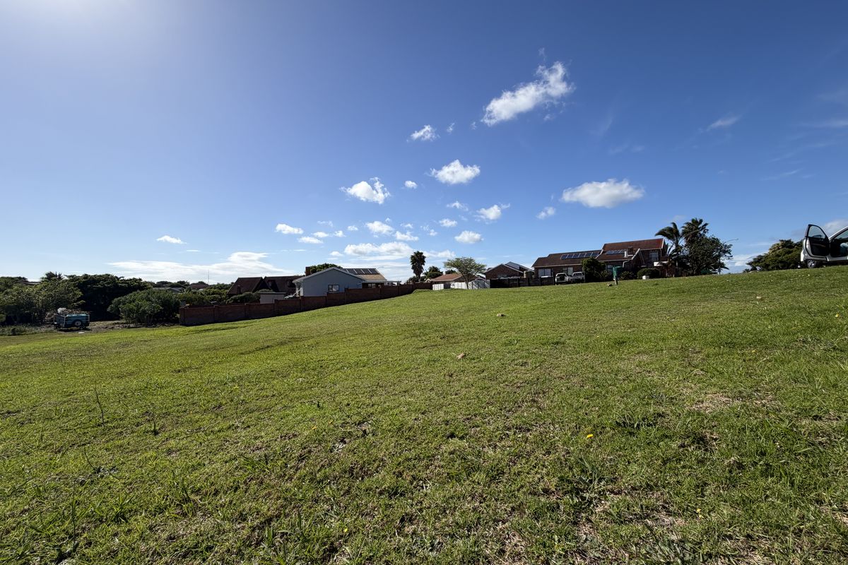 A wide-angle view of a vacant residential plot featuring a grassy lawn and boundary wall, situated in a developed neighborhood.