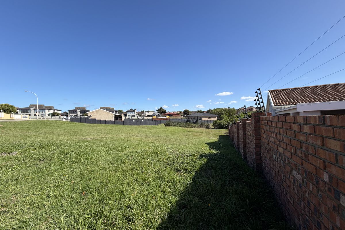 A vacant residential plot featuring a well-maintained brick boundary wall with integrated electric fencing and an open grass area.
