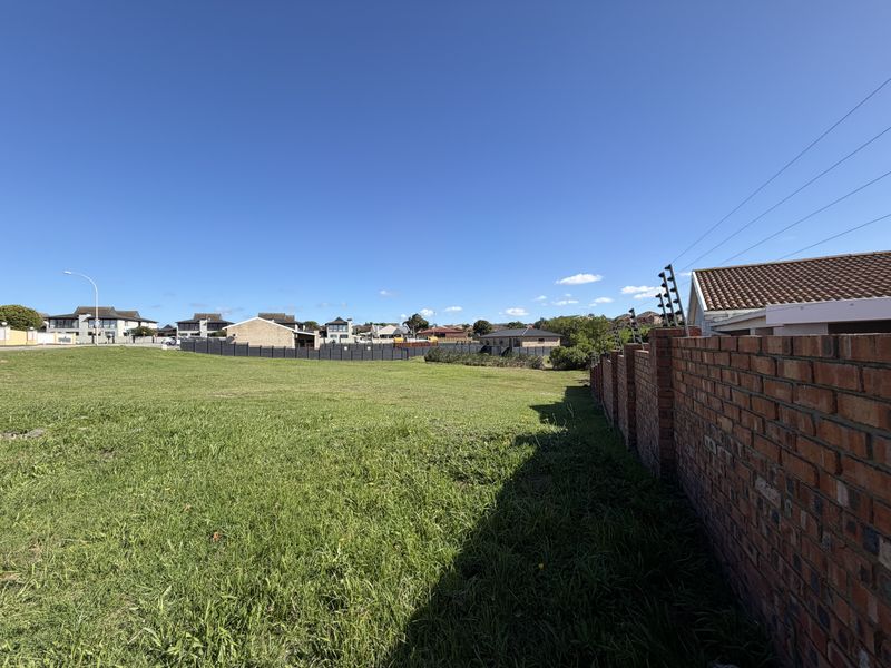 A vacant residential plot featuring a well-maintained brick boundary wall with integrated electric fencing and an open grass area.
