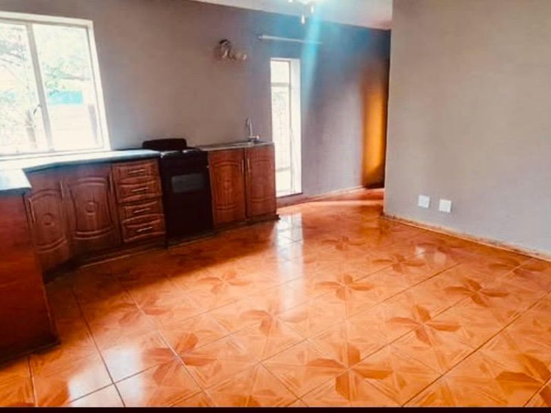 An open-plan living and kitchen area featuring tiled flooring, built-in wooden cabinetry, and a built-in stove, offering a functional and versatile living space.