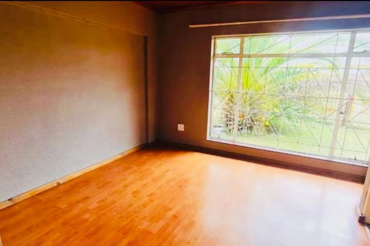 An empty bedroom featuring laminate flooring, a large window with security bars, and neutral wall finishes.