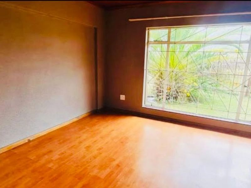 An empty bedroom featuring laminate flooring, a large window with security bars, and neutral wall finishes.