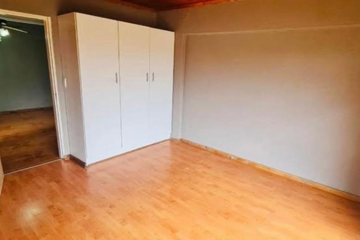 A clean, empty bedroom featuring laminate flooring, a built-in wardrobe, and timber ceiling trim, offering a neutral space ready for personalization.