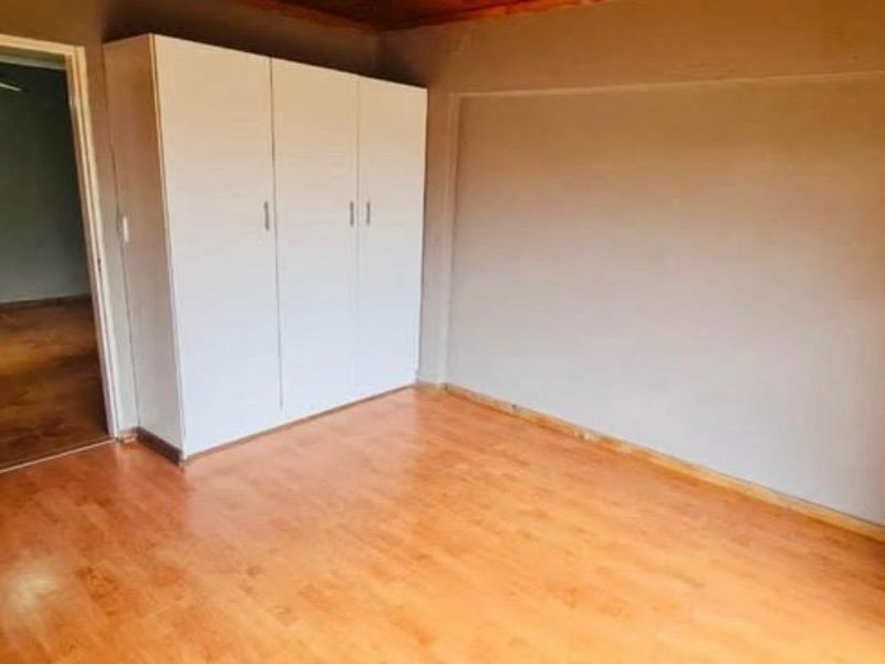 A clean, empty bedroom featuring laminate flooring, a built-in wardrobe, and timber ceiling trim, offering a neutral space ready for personalization.