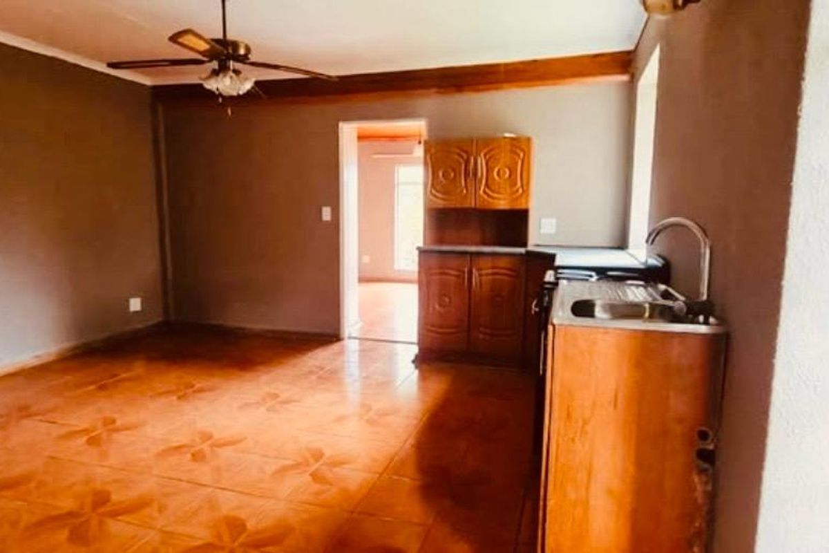 Open plan living and kitchen area featuring tiled flooring, a ceiling fan, and basic wooden cabinetry with a stainless steel sink.