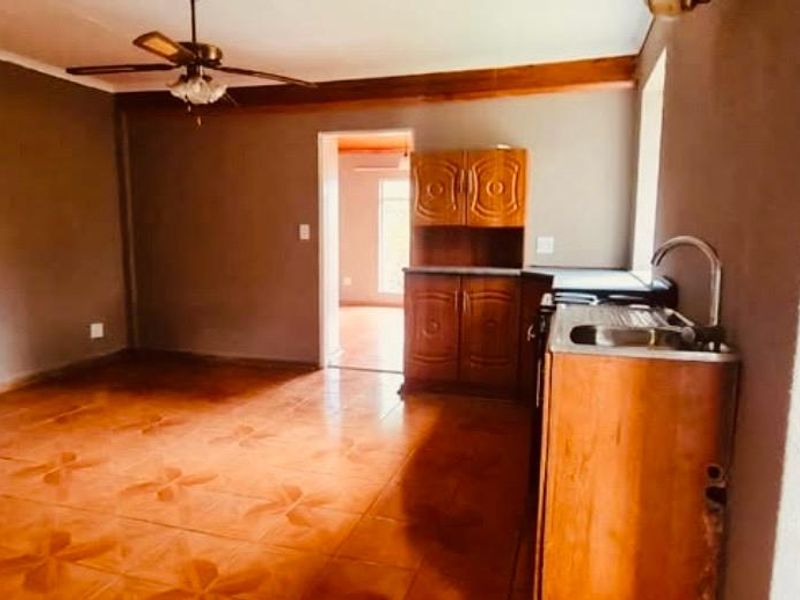 Open plan living and kitchen area featuring tiled flooring, a ceiling fan, and basic wooden cabinetry with a stainless steel sink.
