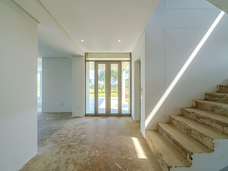 Spacious entrance hall featuring a modern glass door, elevator access, and an unfinished concrete staircase, offering a blank canvas for custom interior finishes.