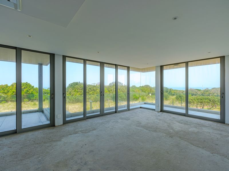 Spacious open-plan living area featuring expansive floor-to-ceiling aluminium sliding doors with panoramic views and access to a balcony.