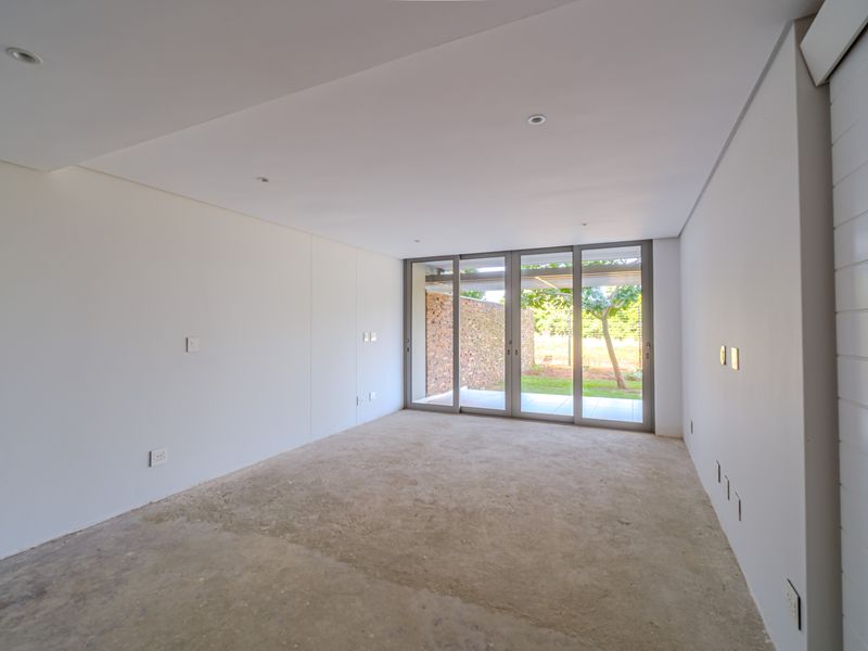 An empty, unfinished bedroom featuring recessed lighting and large sliding glass doors that open to a private garden area.
