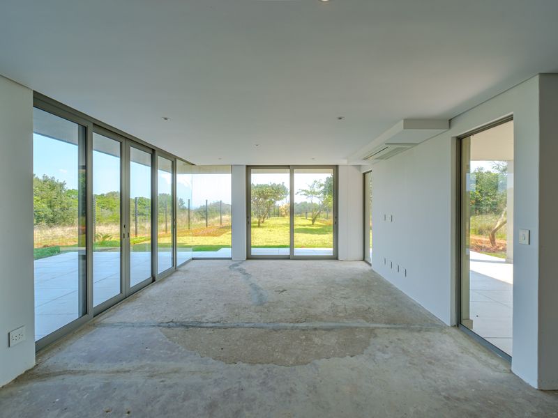Spacious, light-filled living area featuring floor-to-ceiling glass doors with direct access to the patio and garden, currently awaiting final flooring installation.